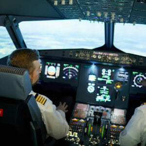 Rear view of modern pilots in uniform with stripes sitting in armchairs and discussing airplane position while flying plane